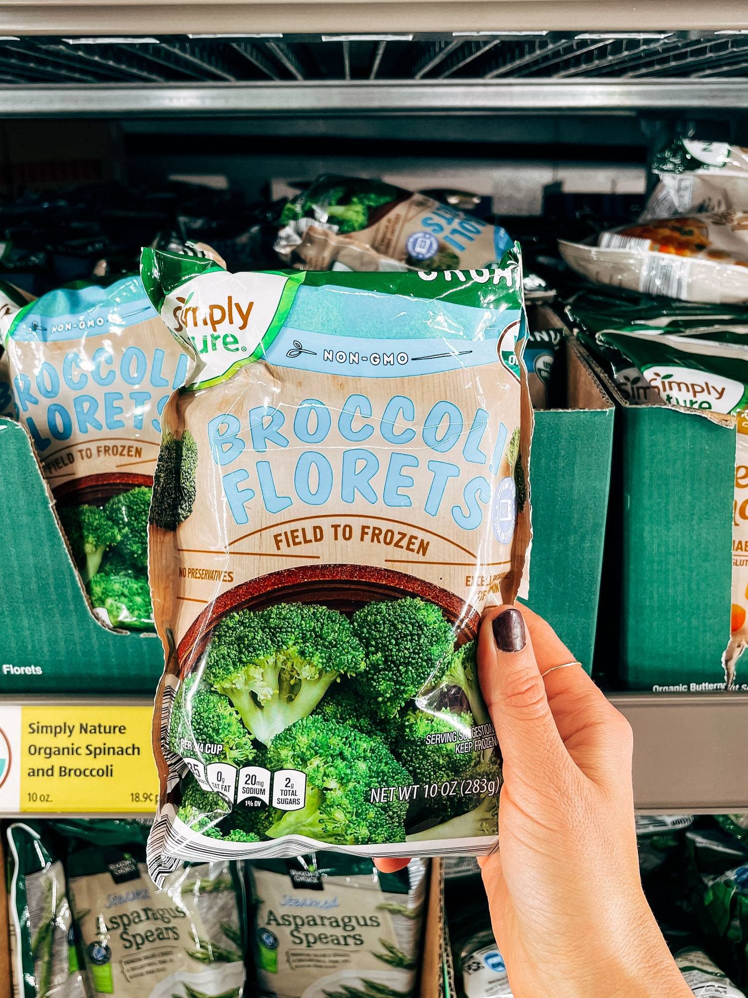 White hand holding a bag of frozen broccoli