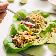 Spoon ladeling lime sauce on the chicken lettuce cups on a plate.